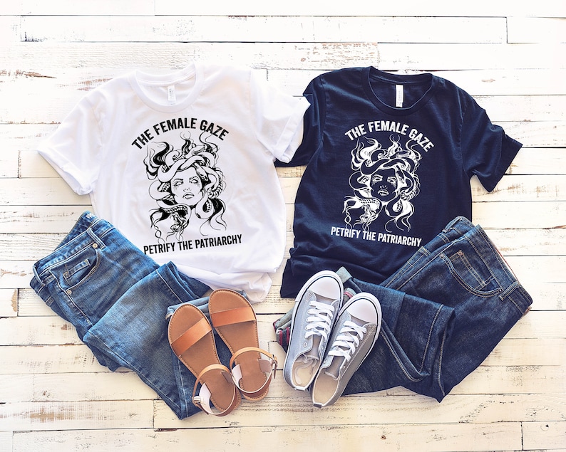 May include: Two t-shirts with a black and white graphic of a Medusa-like figure with snakes for hair. The text on the shirts reads "The Female Gaze" and "Petrify the Patriarchy". One shirt is white and the other is black.