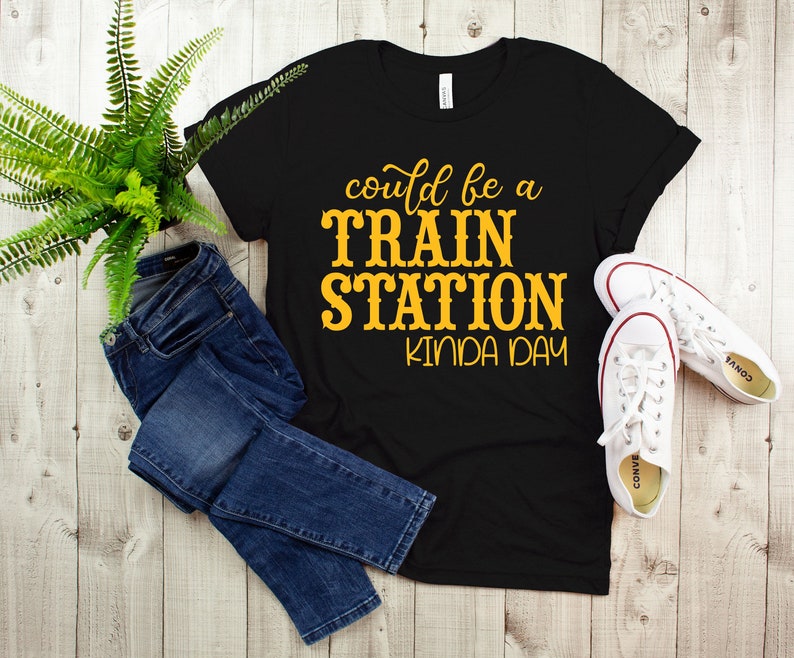 May include: Black t-shirt with the text "could be a TRAIN STATION kinda day" in yellow lettering.