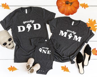 Può includere: Tre magliette grigie con una grafica di un fantasma bianco e il testo "spooky" su ogni maglietta. Le magliette dicono "spooky dad", "spooky mom" e "spooky one".