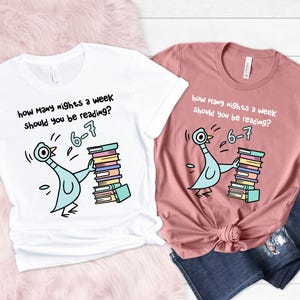 K&ouml;nnte beinhalten: Zwei T-Shirts, eines wei&szlig; und eines rosa, mit einer Cartoon-Taube, die B&uuml;cher h&auml;lt. Der Text lautet: &bdquo;Wie viele N&auml;chte pro Woche solltest du lesen? 6-7&ldquo;.