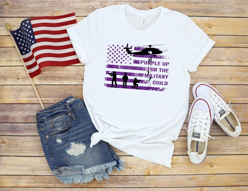 K&ouml;nnte beinhalten: Wei&szlig;es T-Shirt mit einem violetten amerikanischen Flaggen-Design und dem Text "Purple Up for the Military Child".