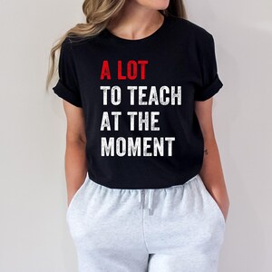 May include: A black t-shirt with white text that reads "A LOT TO TEACH AT THE MOMENT". The word "LOT" is in red.