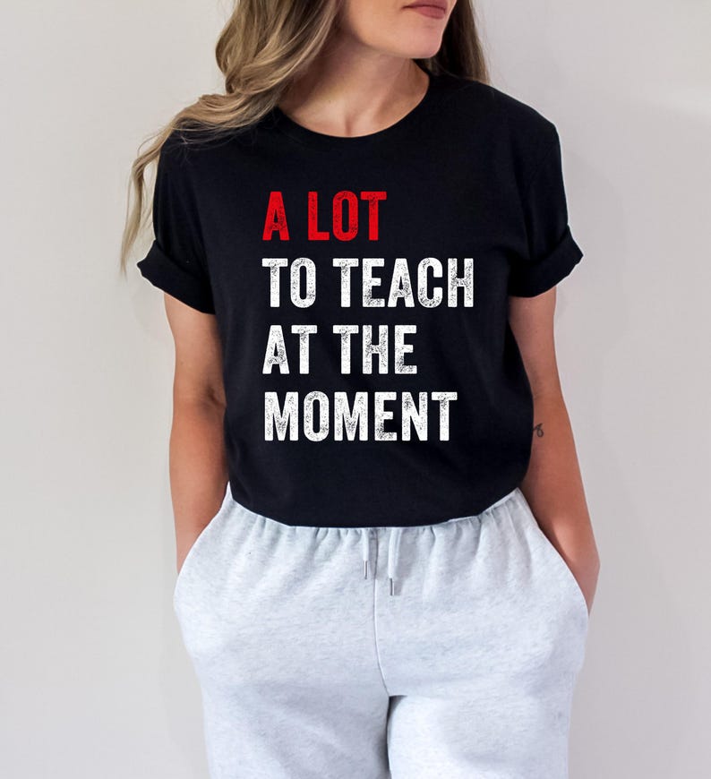 May include: A black t-shirt with white text that reads "A LOT TO TEACH AT THE MOMENT". The word "LOT" is in red.
