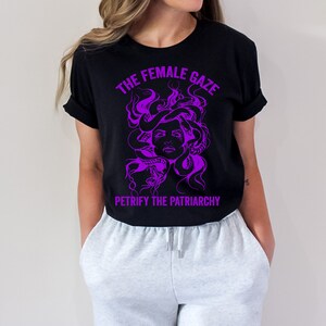 May include: Black t-shirt with a purple graphic of Medusa's head with snakes for hair. The text "The Female Gaze" is above the graphic and "Petrify the Patriarchy" is below.