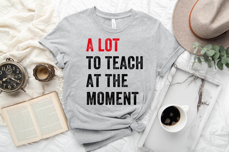 May include: A gray t-shirt with the text "A LOT TO TEACH AT THE MOMENT" in black with the word "LOT" in red.