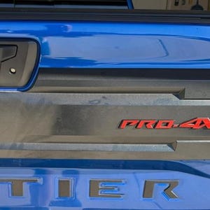 May include: Close-up of a blue vehicle's tailgate with the word "TIER" in silver lettering. The words "PRO-4X" are in red lettering. The tailgate is blue and gray.