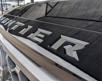 May include: Close-up of a black truck with the word "FRONTIER" in silver lettering on the hood.