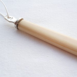 May include: A white ivory handle with a silver metal top. The handle is smooth and has a slight curve.
