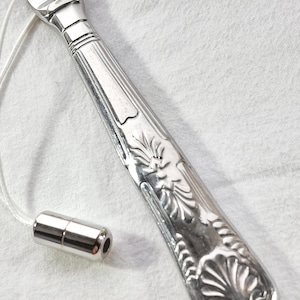May include: A silver light pull with a decorative handle featuring a floral and shell design. The pull has a small cylindrical end piece and a white cord. The handle is approximately 18 cm long.