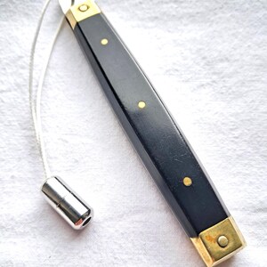 May include: A black pull chain with gold detailing and a silver metal end. The rectangular black handle has gold accents and three gold rivets. A white cord connects the handle to a silver metal pull.