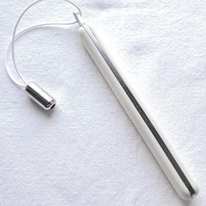 May include: A white, elongated object with a silver stripe down the centre and a silver cylindrical end piece, connected by a white cord. The object is on a white, textured surface.