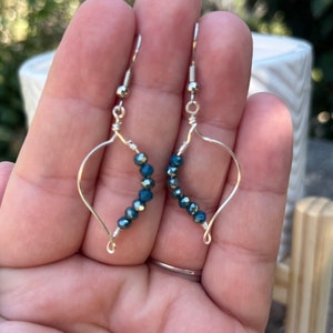 May include: A pair of silver earrings with a teardrop shape and a row of dark blue iridescent beads.