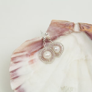 May include: A pair of silver dangle earrings with a pearl and pink beads, displayed on a seashell.