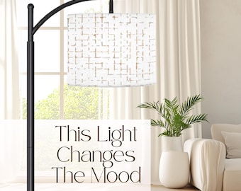 May include: A black metal floor lamp with an arched arm and a cylindrical white lampshade featuring a tan crosshatch pattern. The text "This Light Changes The Mood" is printed in dark brown lettering across the center of the image.