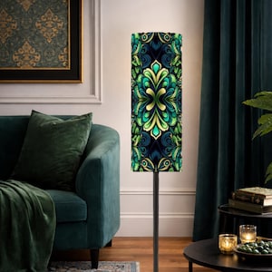 May include: A tall floor lamp with a patterned lampshade. The shade features a symmetrical design in shades of green, blue, and gold. The lamp is set in a living room with a teal sofa and dark green curtains.