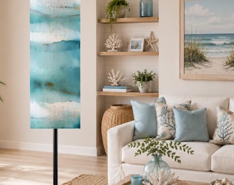 May include: A tall floor lamp featuring a cylindrical shade with a textured, watercolor-style pattern in shades of teal, blue, and white, accented with subtle gold-toned horizontal streaks, supported by a simple, slender black metal pole stand.