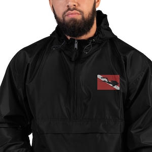 Könnte beinhalten: Eine schwarze Windbreaker-Jacke mit Reißverschluss und einem Taucherflaggen-Logo auf der Vorderseite. Die Flagge ist rot mit weißem Rand und einer Silhouette eines Tauchers.