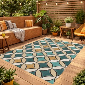May include: An outdoor rug with a geometric pattern in teal, beige, and cream colors. The rug is rectangular and placed on a wooden deck, surrounded by plants and outdoor furniture. The design features interlocking oval shapes.