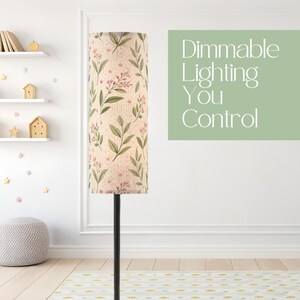May include: A tall floor lamp with a cylindrical shade featuring a botanical print of green leaves and small pink flowers on a beige background. The text Dimmable Lighting You Control is displayed in white on a light green rectangular background.