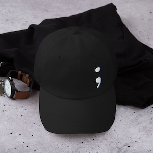 May include: Black baseball cap with a white semicolon embroidered on the front.