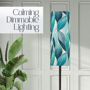May include: A tall floor lamp with a cylindrical shade featuring a pattern of blue and teal leaves. The lamp has a black metal pole and the text "Calming Dimmable Lighting" is displayed on a white rectangle.