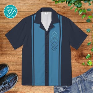 May include: Short-sleeved button-up shirt in navy blue with a light blue center panel and vertical stripes. The shirt features a geometric diamond design and a classic collar. The shirt is displayed on a wooden surface.
