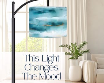 May include: A black floor lamp with a square lampshade featuring an abstract watercolor design in shades of blue and gold. The text on the image reads: "This Light Changes The Mood."