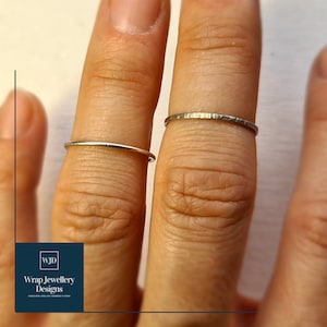 May include: Two silver rings on a person's fingers. The ring on the index finger is plain and the ring on the middle finger has a hammered texture.
