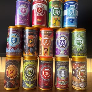 Op de afbeelding: Een verzameling van vijftien cilindrische drankblikjes gerangschikt in drie rijen, elk met unieke kleurrijke grafische labels met verschillende logo's en teksten zoals Juggernog, Speed Cola, Quick Revive, Deadshot Daiquiri en Tombstone Soda.