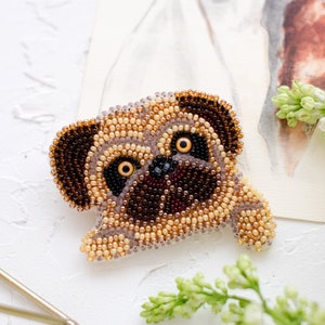 Può includere: Un broche di un carlino in perline marroni, beige e nere. Il carlino guarda a destra con la lingua di fuori.