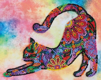 Può includere: Una silhouette di gatto colorata realizzata con perline su una tela tie-dye arcobaleno. Il gatto è in una posa allungata con la coda arrotolata sulla schiena. Le perline sono disposte in un motivo floreale.