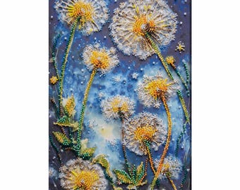 May include: A close-up of a beaded art piece depicting a cluster of white dandelions with yellow centers against a blue background. The dandelions are arranged in a vertical line, with the largest dandelion at the top and the smallest dandelion at the bottom.
