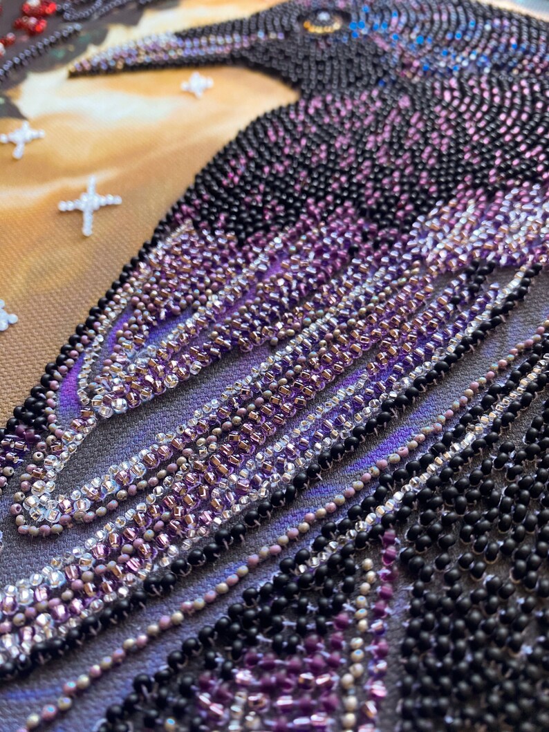 Puede incluir: Primer plano de una obra de arte con cuentas que representa un cuervo con cuentas negras, moradas y plateadas. Las cuentas est&aacute;n dispuestas en un patr&oacute;n que crea una sensaci&oacute;n de profundidad y textura.