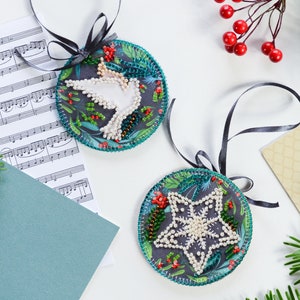 May include: Two round Christmas ornaments with a green and blue background. One ornament features a white dove and the other features a white snowflake. Both ornaments are decorated with red and white beads.