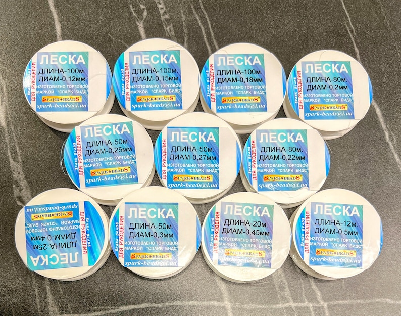 May include: A collection of white spools of fishing line, each labeled with the text "LESKA" and details about the length and diameter of the line in millimeters. The spools are labeled in Russian.