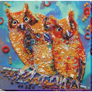 May include: Two orange and brown owls with colorful bead embellishments on a blue background. The owls are facing each other and have their wings spread out.