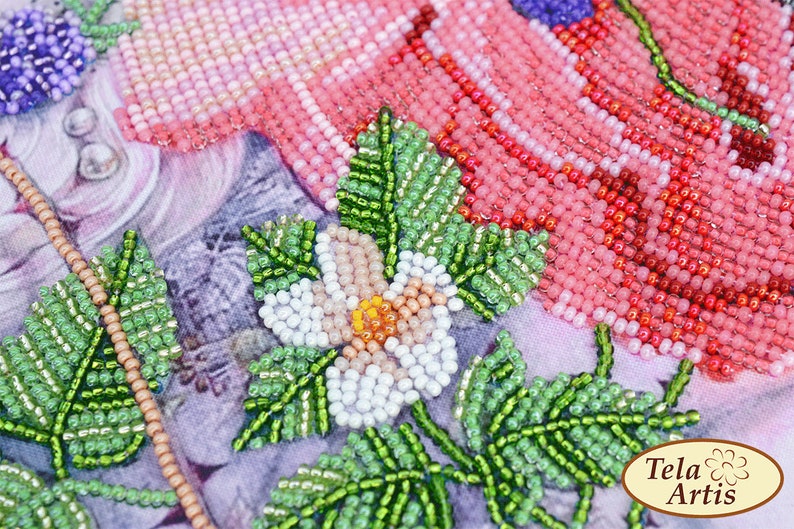 K&ouml;nnte beinhalten: Nahaufnahme eines Blumenmusters aus Perlen mit rosa, wei&szlig;en, gr&uuml;nen und orangefarbenen Perlen. Die Blume ist von gr&uuml;nen Bl&auml;ttern umgeben. Das Muster befindet sich auf einem Stoffhintergrund mit dem Text "Tela Artis" in der unteren rechten Ecke.