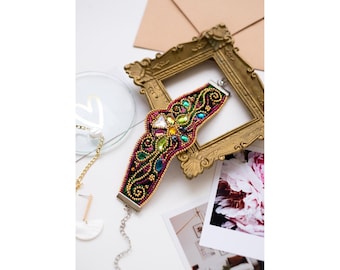 May include: A colorful beaded bracelet with a floral design and a silver clasp. The bracelet is made with a variety of beads, including clear, green, blue, and pink beads. The bracelet is displayed on a white surface with a gold picture frame.