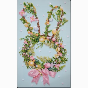 May include: A beaded wreath in the shape of a bunny rabbit with pink, green, yellow, and white beads. The wreath is decorated with a pink bow.