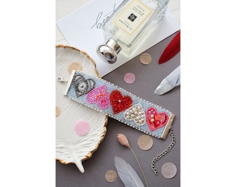 May include: A blue beaded bracelet with a silver clasp and a row of colorful beaded hearts. The hearts are red, pink, and white with pearl accents.
