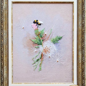May include: A framed beaded artwork depicting a dandelion with a bumblebee perched on a pink flower. The dandelion is white with a brown center and has delicate white seeds. The background is a soft pink.