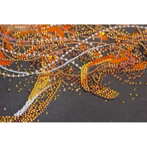 May include: Close-up of a beaded artwork with a design of swirling lines and shapes. The beads are in shades of orange, yellow, and white, creating a textured and intricate pattern.