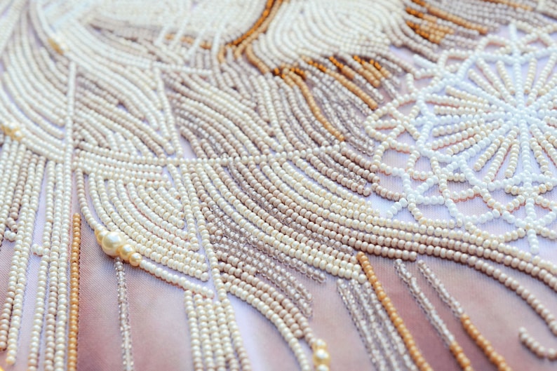 May include: Close-up of a beaded fabric with a white, cream, and gold pattern. The beads are arranged in a geometric design, creating a textured and intricate surface.