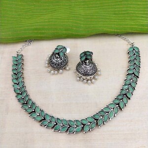 May include: A silver necklace with green leaf-shaped pendants and matching earrings. The earrings are jhumka style with a pearl drop.