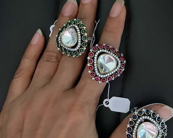 May include: Three silver rings with a teardrop-shaped clear stone surrounded by smaller stones. The rings have different colored stones around the center stone: green, red, and blue.