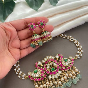 May include: A gold necklace with a peacock design featuring pink and green gemstones. The necklace has a pearl and green gemstone drop. Matching earrings with pink and green gemstones are also included.