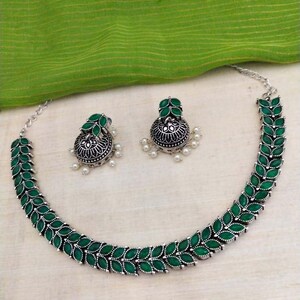 May include: A silver necklace with green gemstone leaves and matching earrings. The necklace and earrings have a traditional Indian design.