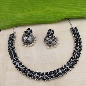 May include: A silver necklace with black leaf-shaped stones and matching earrings. The earrings are dangle style with a pearl drop.