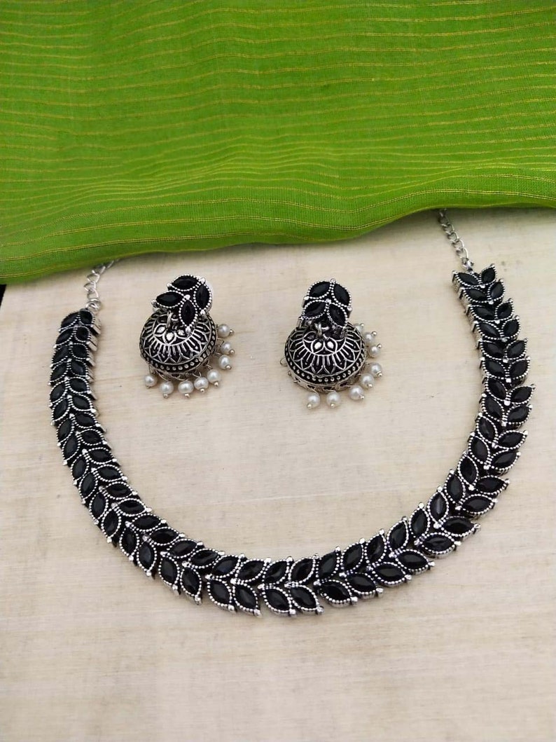 May include: A silver necklace with black leaf-shaped stones and matching earrings. The earrings are dangle style with a pearl drop.