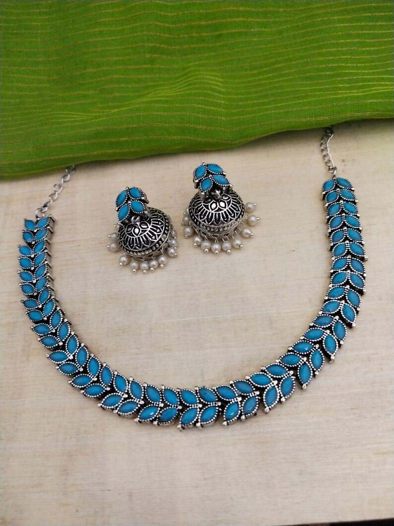 May include: A silver necklace with a blue stone leaf design and matching earrings. The earrings have a pearl drop.